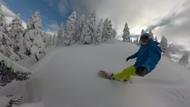 SELFIE: Active young man on a fun snowboarding descent among snowy spruce trees. Snowboarder enjoys riding on freshly snowed untouched terrains during adventurous heliboarding trip in Albanian Alps.