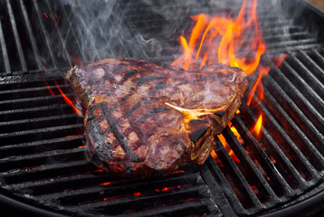 Barbecue dry aged wagyu porterhouse beef steak grilled as close-up on a charcoal grill with fire and smoke