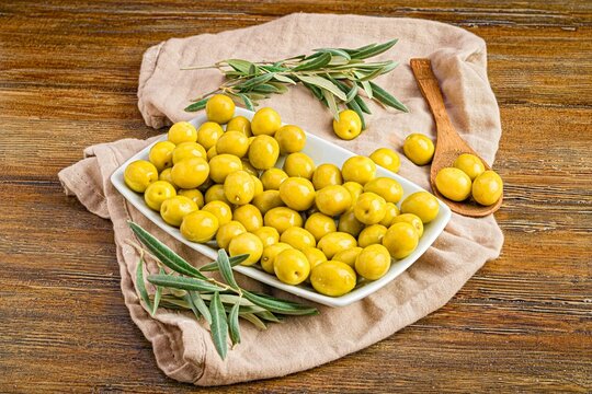 Cheerful still life featuring a white bowl of freshly-picked Manzanilla Olives and rosemary leaves