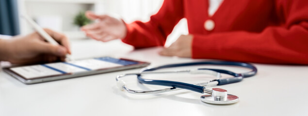 Focused stethoscope on office desk with blurred background of patient attending to doctor...
