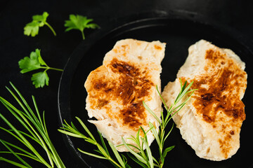 Chicken fillets fried until half cooked,product.Quick cooking at home.Semi-finished chicken fillets,lightly fried,on a dark background with fresh herbs.Half-finished.Quick cooking at home.Fast food.