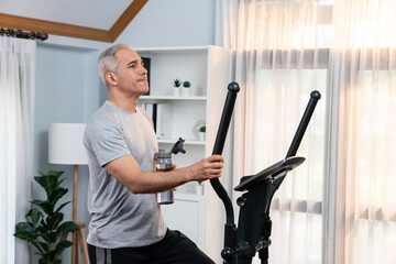 Active senior man running on elliptical running machine and drinking water at home portrait as fitness healthy lifestyle and body care after retirement for pensioner. Clout