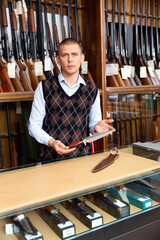 Portrait of gun shop owner demonstrating hunting dagger with double edged blade and wooden handle