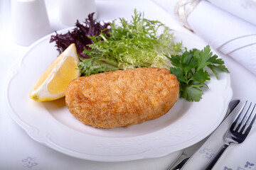 fried cutlet with lettuce lies on a white plate on a white dining table