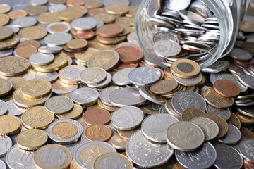 Various coins are falling out of a glass jar, concept of saving money.