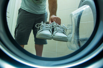 View from inside the washing machine of an unknown person putting dirty and old sneakers into the washing machine for washing
