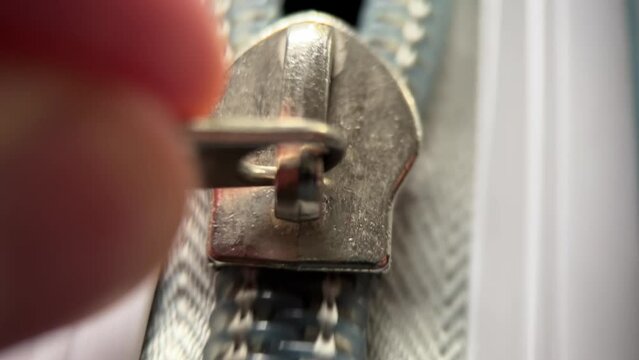 Man's hand opens the zipper of a grey polycarbonate travel suitcase. Extreme close-up