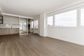 Empty living room with large windows and open kitchen at the back with retractable glass screen