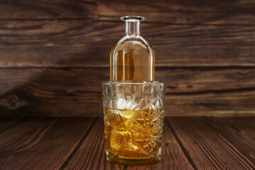 A bottle with liquor next to a carved glass filled with liquor and ice on a dark wooden surface