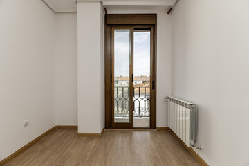 empty room with white painted walls and light wooden floors and access to a balcony with sliding aluminum and glass doors