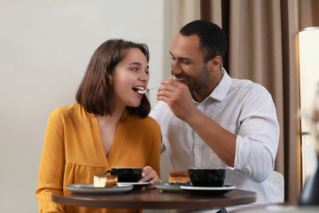 Romantic date. Guy feeding his girlfriend with cheesecake in cafe
