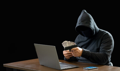 Hacker spy man oneperson black hoodie sitting on table hand holding gun threaten looking computer laptop used login password attack security data digital internet network system, night dark background