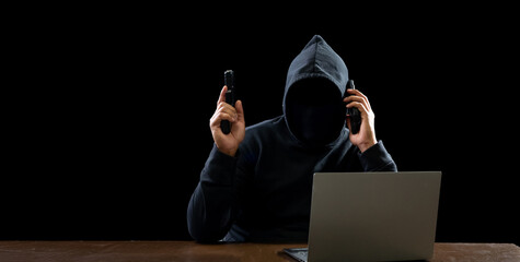Hacker spy man oneperson black hoodie sitting on table hand holding gun threaten looking computer...
