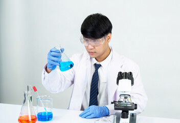 Fototapeta premium Portrait asian man student scientist Wearing a doctor gown in the lab looking hand at chemist. caused by mixing reagents in scientific research laboratories with test tubes and microscope on the table