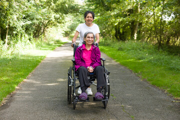 Elderly Indian woman outdoors in a wheelchair with carer, UK