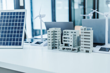 A model city tower or apartment with buildings, solar panel, and wind turbines shows clean energy...