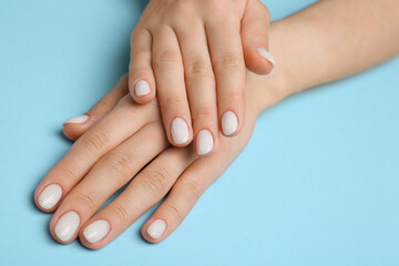 Woman showing her manicured hands with white nail polish on light blue background, closeup