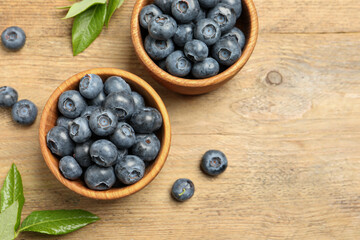 Bowls of fresh tasty blueberries and leaves on wooden table, flat lay. Space for text