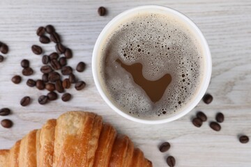 Coffee to go. Paper cup with tasty drink, croissant and beans on white wooden table, flat lay