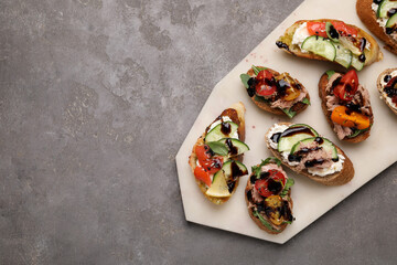 Delicious bruschettas with balsamic vinegar and different toppings on grey textured table, top view. Space for text