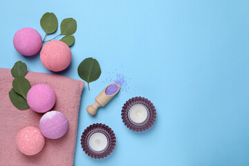 Bath bombs, eucalyptus leaves, burning candles and sea salt on light blue background, flat lay. Space for text
