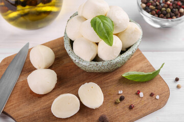 Tasty mozzarella balls, basil leaves and spices on white wooden table, closeup