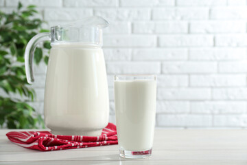 Jug and glass of fresh milk on white wooden table, space for text