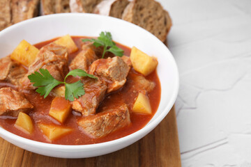 Fototapeta premium Delicious goulash in bowl on white textured table, closeup