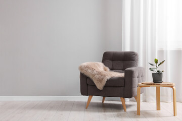 Comfortable armchair, side table and houseplant near light grey wall indoors. Space for text