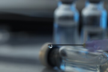 Drop of medication on syringe needle against blurred background, closeup. Space for text