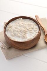 Fototapeta na wymiar Tasty boiled oatmeal in bowl on white wooden table
