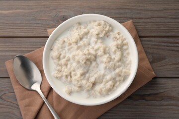 Tasty boiled oatmeal in bowl and spoon on wooden table, top view