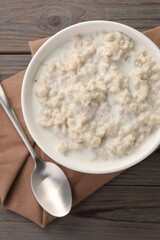 Tasty boiled oatmeal in bowl and spoon on wooden table, top view