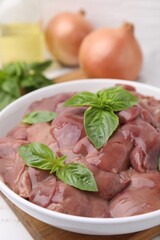 Bowl with raw chicken liver and basil on table, closeup