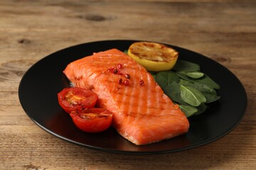 Tasty grilled salmon with tomatoes, lemon and basil on wooden table, closeup