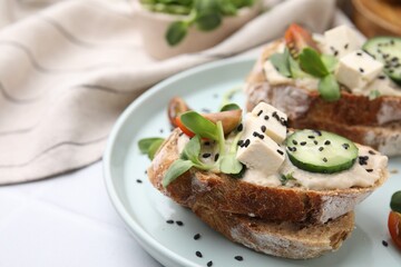 Tasty vegan sandwiches with tofu, cucumber, tomato and sesame seeds on white tiled table, closeup