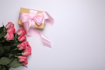 Gift box wrapped with pink bow and beautiful flowers on white background, flat lay. Space for text