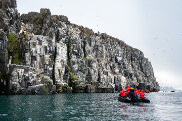 Small boats of tourists watching Brunnich's Guillemots nesting on bird cliffs on Mount Guillemot on Nordauslandet in the Hinlopen Straight, arctic tourism expedition around Svalbard
