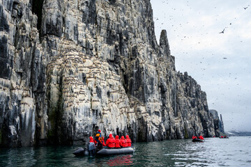 Small boats of tourists watching Brunnich's Guillemots nesting on bird cliffs on Mount Guillemot on Nordauslandet in the Hinlopen Straight, arctic tourism expedition around Svalbard  © knelson20