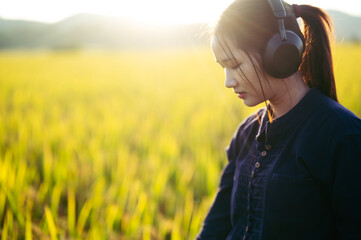 Woman wearing headphones listening to music breathing fresh air relaxing stand on rice field sunset