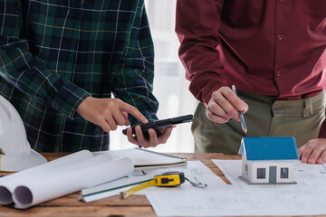 A group of engineers and architects are discussing the structure of a house building inside an office conference room.