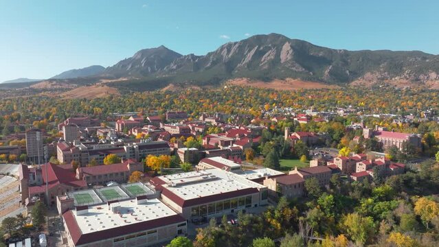 Aerial view of CU Boulder campus and Folsom football field surrounded by green and yellow fall trees with the rocky flatiron mountains in the background in the front range of Colorado panning left