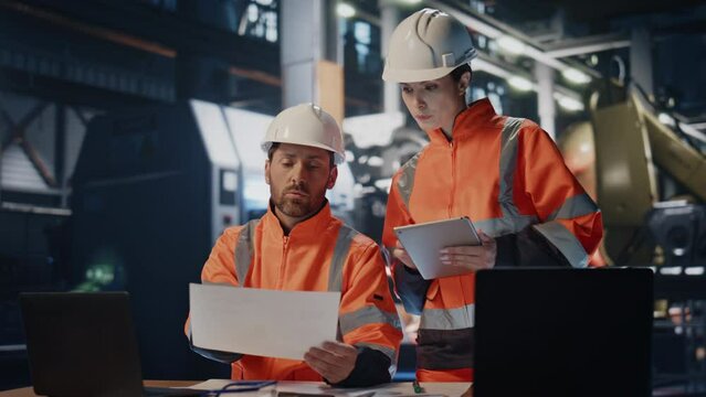 Two busy engineers working in industrial workshop. Woman technician looking 
