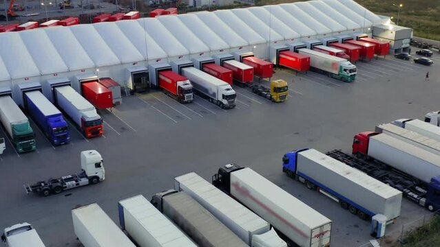 Aerial view of semi-trailers trucks stand in the truck stop and at a warehouse ramps for unloading and loading goods in a logistics park