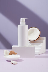 Lotion pump bottle without label is placed on a round podium, fresh coconuts are placed on a podium simulating stairs. Fresh coconut is a popular ingredient in the beauty industry.