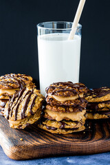 A pile of chocolate and caramel lace cookies with a tall glass of cold milk.