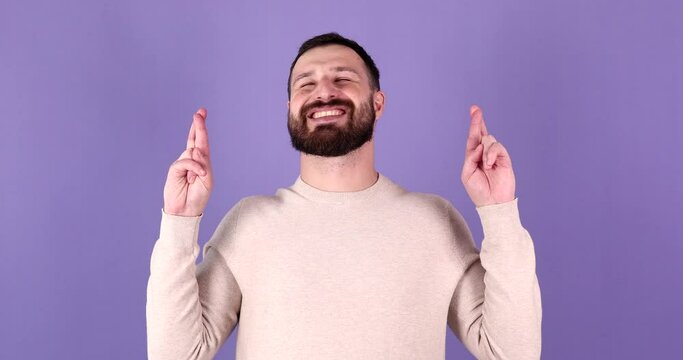 Young bearded man hold hands folded in prayer beg about something making wish keep fingers crossed isolated on purple background studio portrait.