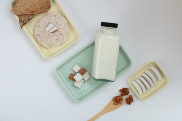 Top view of an unlabeled nut milk bottle, fresh coconut, and coconut shells are placed on various-sized rectangular plates. Coconut milk provides essential minerals such as potassium and magnesium.