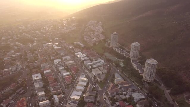 Aerial view, city and buildings, mountain and neighborhood outdoor, urban development and property in Cape Town. Drone, architecture and cityscape, houses and infrastructure at sunset on landscape