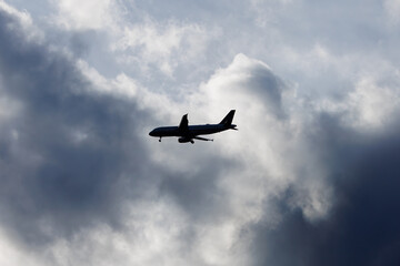 Fototapeta na wymiar Silhouette of an airplane with its landing gear coming down ready to land with a cloudy background